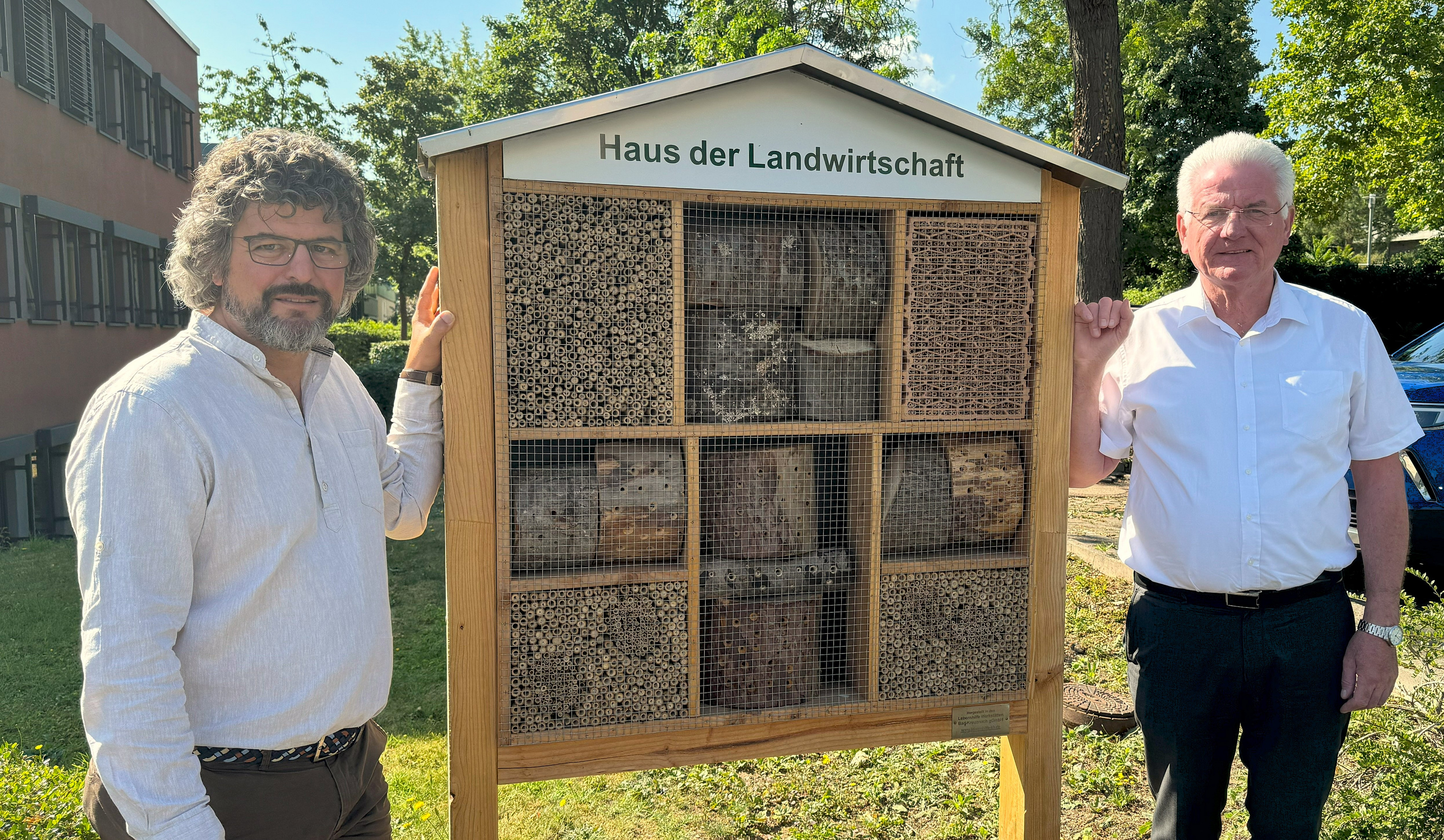 Zwei Männer neben einem Insektenhotel.