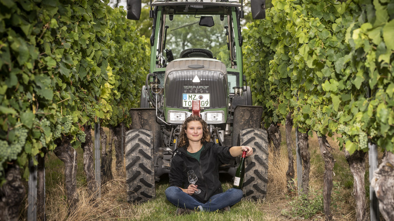 Frau im Wingert mit Traktor und Weinflasche.