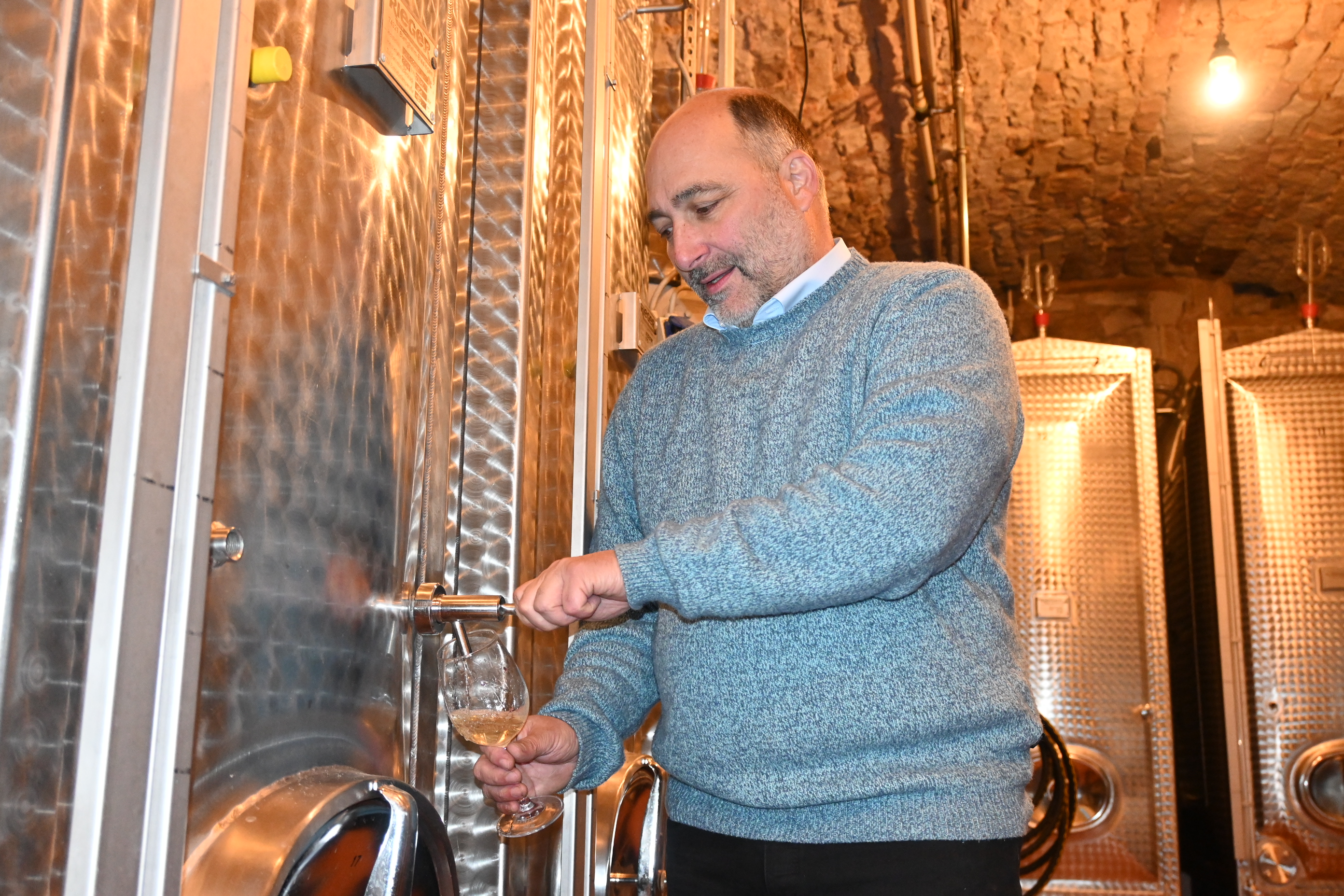 Winzer zapft Wein in ein Glas vom Stahltank.